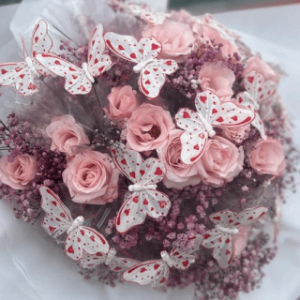Buquê com rosas rosa claro, flores lilases e decoração com borboletas artificiais.