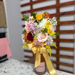 Arranjo floral com flores coloridas em garrafa de espumante para presente especial em Goiânia